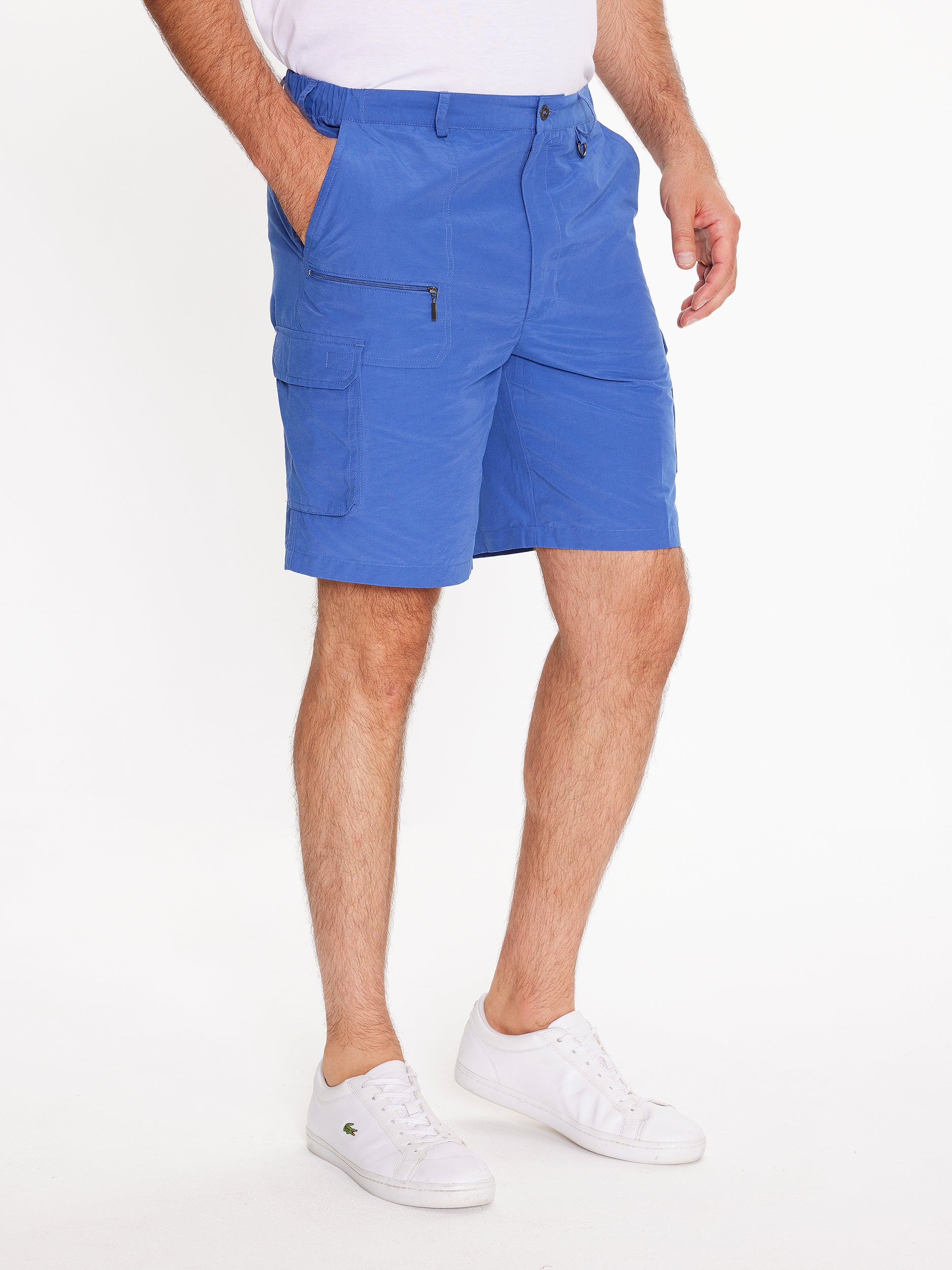 Side image of model wearing the mens Woodbury Short in blue. Short is knee length, has button fly, belt loops, side cargo and slanted pockets, and a front zip pocket.Model has hand in side pocket.