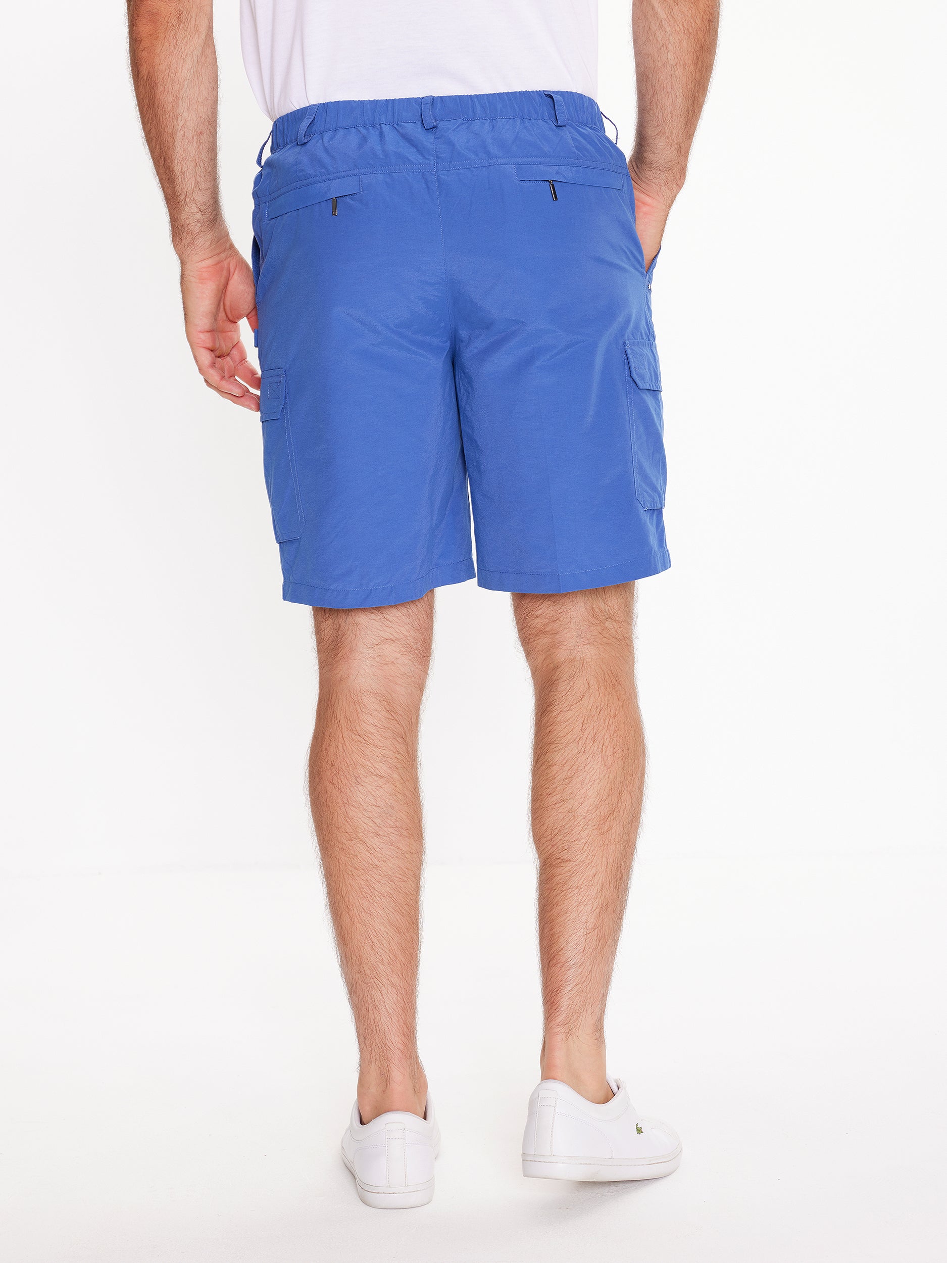 Back image of model wearing the mens Woodbury Short in blue. Short is knee length, has button fly, belt loops, side cargo and two back zip pockets. Model has hand in side pocket.