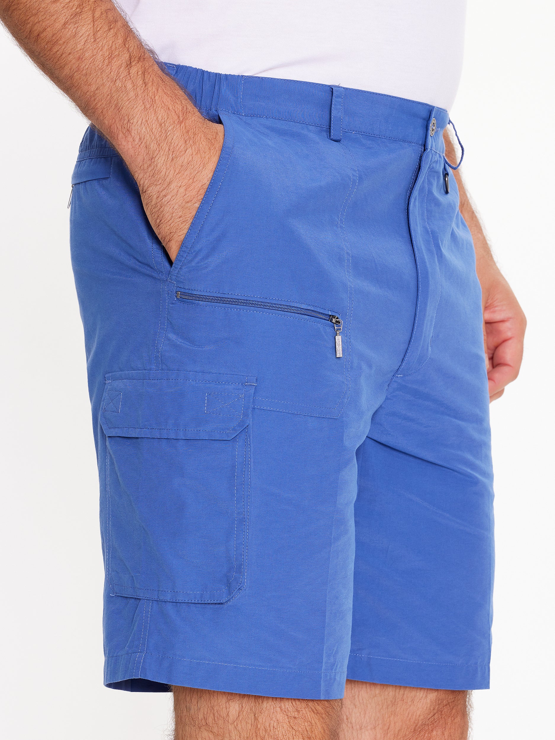 Close up side image of model wearing the mens Woodbury Short in blue. Short is knee length, has button fly, belt loops, side cargo and slanted pockets, and a front zip pocket.